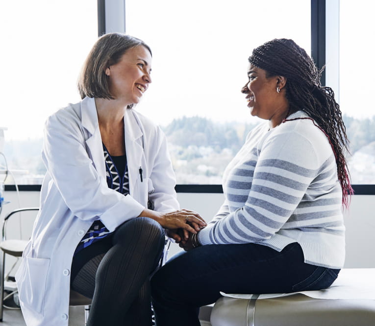Female doctor and patient smiling and talking together in a bright medical office.