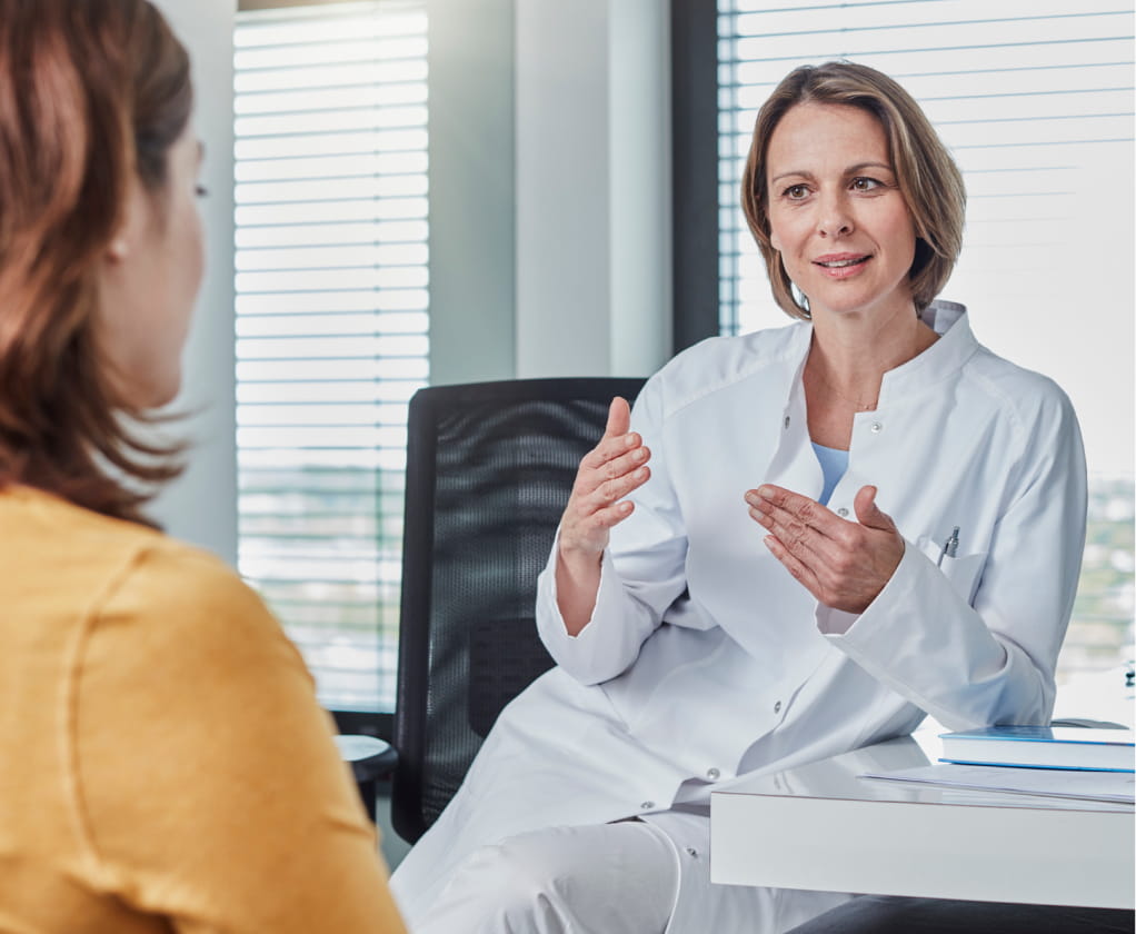 Female doctor in a white coat consults with a patient in an office setting.